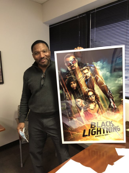 Man poses with movie poster for Black Lightning